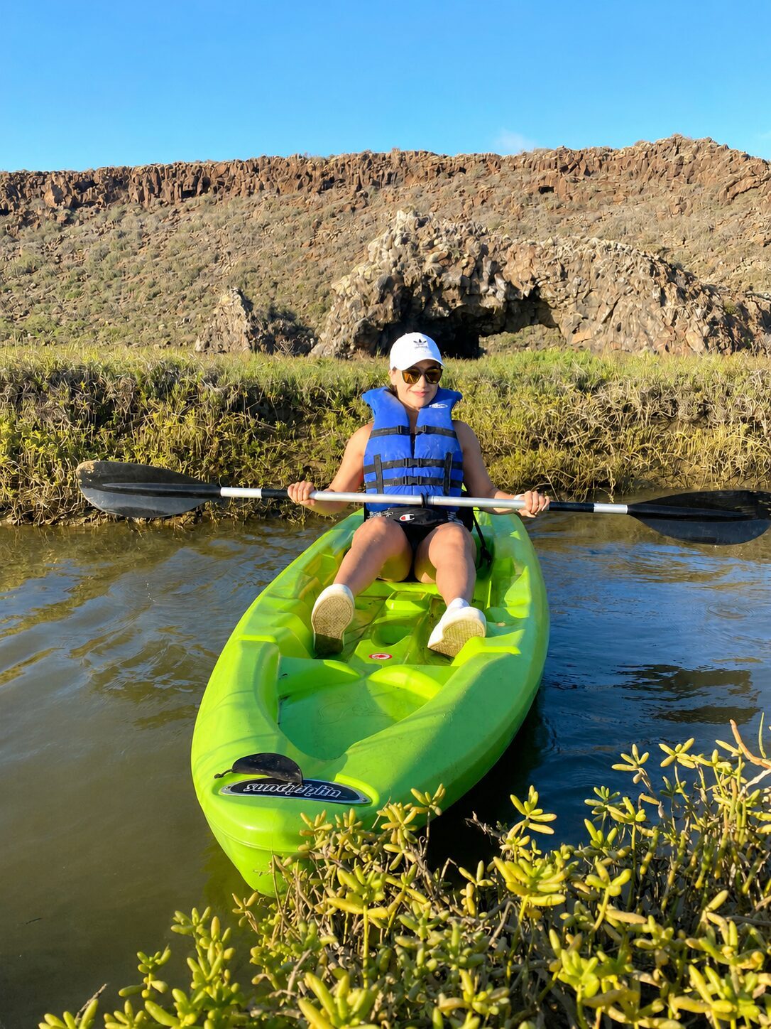 Remando en kayak por un canal del humedal frente al arco de roca